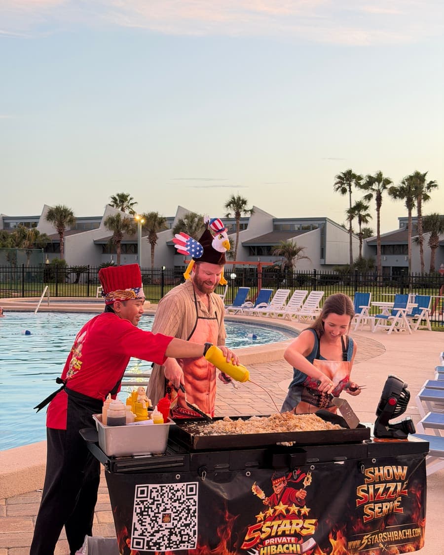 Chef cooking on the flat-top while two guests in novelty hats watch from the poolside