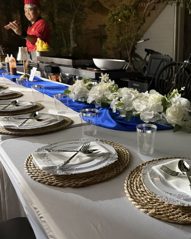 Courtyard table laid with white florals, chargers and cutlery, bicycles parked against the wall behind