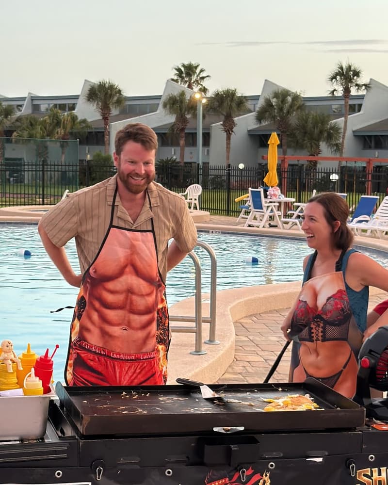 Two guests in novelty aprons standing at the hibachi flat-top beside a resort pool